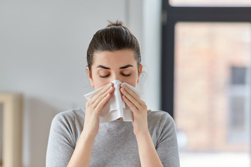 healthcare, cold, allergy and people concept - sick woman blowing her runny nose in paper tissue at...