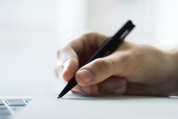 Businessman writes with a pen in diary on laptop keyboard in a sunny office, business and education concept. Close up