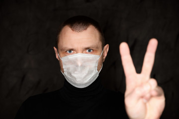 Portrait of a man in a medical mask shows his fingers on a black background