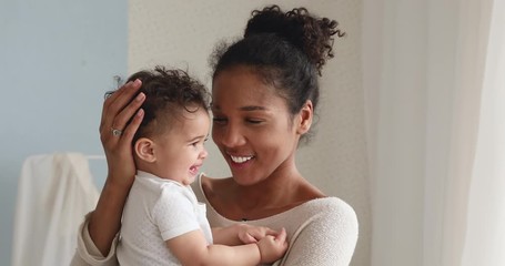 Smiling african american mum holding cute small infant boy son, cuddling and playing together at home. Loving young mother embracing funny little cute baby girl daughter enjoying sweet tender moment. - Powered by Adobe