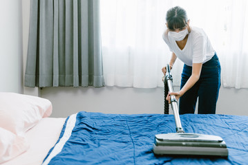 Woman using vacuum cleaner with bed room in background.  With copy space.