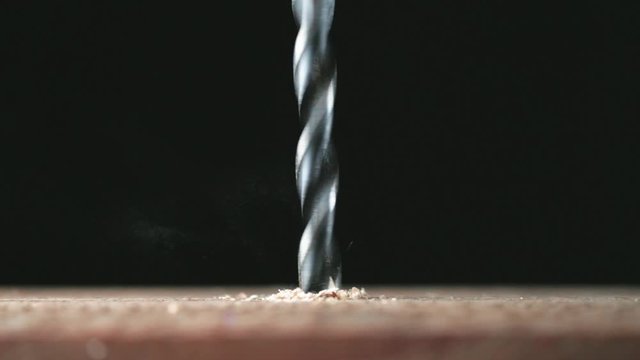 Electric drill bit drills a hole in the board. Joinery and construction work close up. Wood chippings fly off a metal drill. Handyman bores holes into a wooden board.  