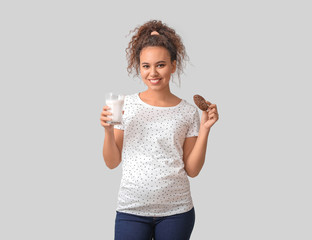 Young pregnant African-American woman with milk and cookie on light background