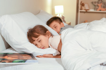 Little girl with brother sleeping in bed at night