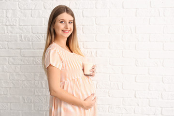 Beautiful pregnant woman with milk on white brick background