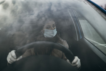 Young woman in a mask and gloves driving a car.