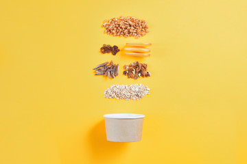 Healthy breakfast concept, paper bowl with granola, nuts, wheat on color background, morning meal...