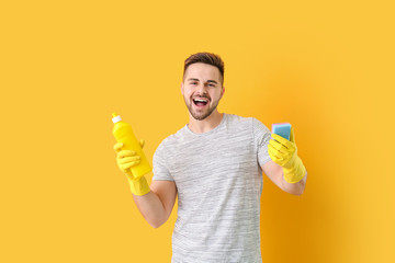 Happy man with detergent and sponge on color background