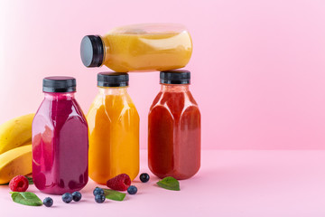 Colourful healthy smoothies and juices in bottles on color background with copy space.