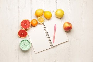 Notebook with fresh fruits and clock on table