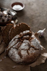 Sliced rye bread with garlic and olive oil on craft paper on a dark brown background. Homemade baking. Close-up, copy space.