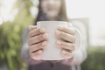 Close up of women's hands holding white mug. Gray knitted sweater.