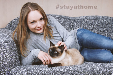 young woman staying at home with cat as social distancing measure during corona crisis - hashtag stayathome