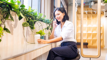 Co working space concept. A young woman is working in a common area. Women are using mobile phones...