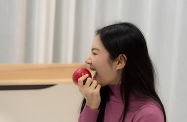 Young Asian beautiful woman enjoy eating red apple on bed with happy mood in bedroom at night time