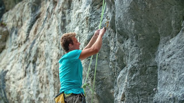 Young athletic man practicing rock climbing on a steep high wall with ropes and other equipment.