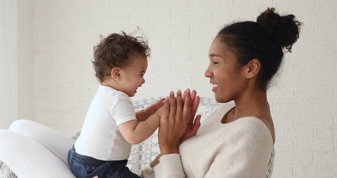 Adorable infant baby girl daughter playing patty cake with african mom at home. Happy mixed race family mother and cute little boy son learning funny game having fun enjoying sweet moments together.