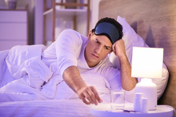 Obraz premium Young man taking pills for insomnia in bedroom
