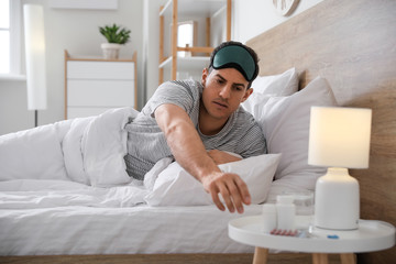 Young man taking pills for insomnia in bedroom