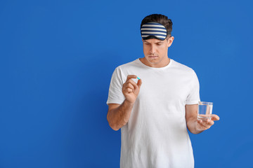 Young man with sleeping pills and glass of water on color background