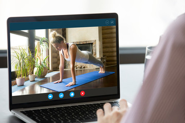 Focus on computer screen with fit young woman standing in plank position, enjoying practicing yoga...