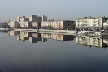 Fototapeta premium Buildings of the Frunze Embankment in Moscow are reflected in the smooth blue water of the Moscow River. Early spring, sunny day.