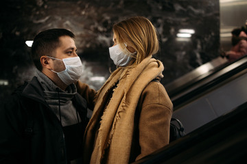 Man and woman in medical masks on escalator in subway.