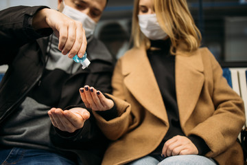 Man and woman using antiseptic while sitting in subway car.