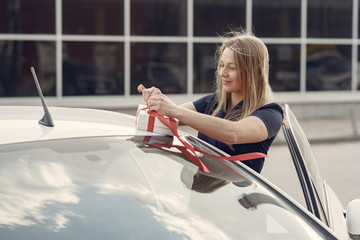 Woman by the car. Lady in a blue dress. Woman holds the box in her hands.