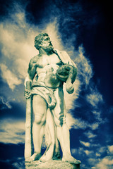Ancient stone statue of Hercules against dramatic view of cloudy sky as symbol of power and strength.