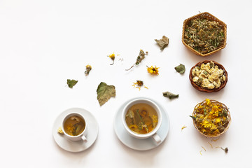 Obraz na płótnie Canvas Top view of two cups of hot healing herbal tea for cough and coronavirus from dried leaves of currant, calendula flowers, chrysanthemum and cinquefoil on a white background. Copy space, flat lay