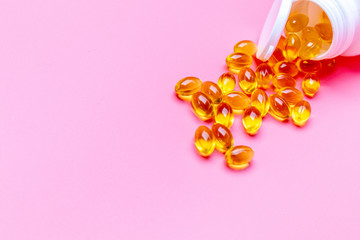 Dietary supplement gel capsules. pills spilling out of prescription bottle on pink background.