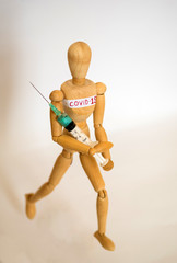 COVID-19 Pandemic Coronavirus concept ; Close-up of a wooden model man is carrying syringe. Corona virus vaccine on the way.