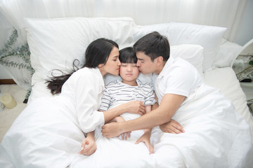 Obraz na płótnie Canvas Young asian mother, father and boy sleeping in bed, mom and dad kiss on cheek of son,view from above