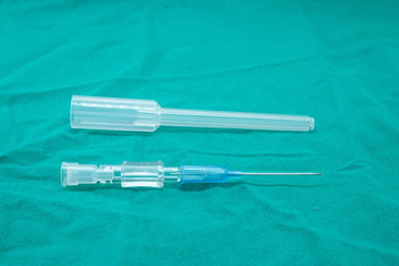 IV catheter with a sterile blue needle Coupled with a needle sheath placed on a green cloth.