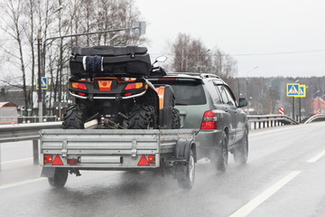 Driving safety on a wet slippery road with a single-axle trailer — SUV car fast carries a Quad bike after rain, aquaplaning dangerous © Ilya