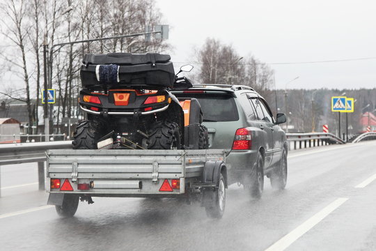 Driving safety on a wet slippery road with a single-axle trailer &mdash; SUV car fast carries a Quad bike after rain, aquaplaning dangerous