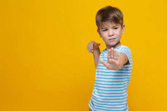 Little cute boy in striped clothes holds out his hand forward in a barrage gesture isolated on a yellow background.
