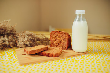 Sliced dark bread and fresh milk bottle on yellow table. Healthy nutrition, healthy food on the table. White milk bottle and fresh bread.