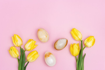 Stone Easter eggs and beautiful yellow tulips. Minimal style composition with Easter concept. Spring blossom flowers. Top view and copy space.