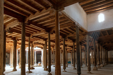 Fototapeta premium Main hall of Juma mosque (10th and 18th centuries) with old wooden pillars and sunbeams from the window. Khiva, Uzbekistan, Central Asia.