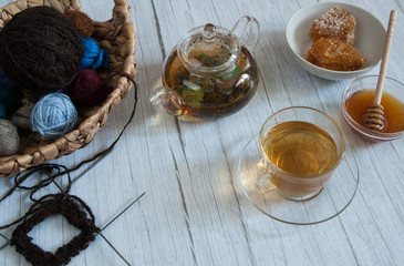 Fototapeta na wymiar Free time. I'm learning to knit. Balls of wool yarn in a basket, the beginning of knitting on four needles, green tea in a teapot and golden honey on a light wooden background.