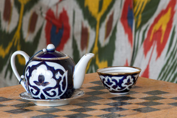 Teapot and tea cup on a table stylized as a chessboard in authentic uzbek interior. Traditional uzbek cafe. Uzbekistan, Central Asia.