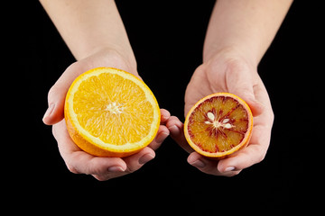 Orange and blood or red orange fruit halves in hands on black background