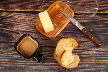 Fresh wheat toast with butter, butter in a wooden butter dish, a knife with a wooden handle and a Cup of coffee with milk on a wooden background. Close up.