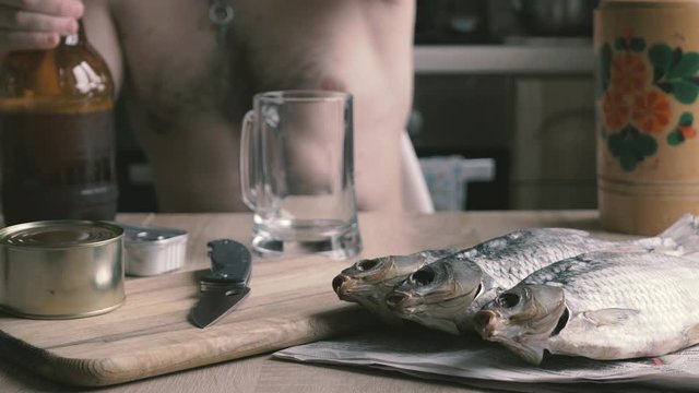 Brutal man pouring bottle of beer into glass and drinking. Glass of cold fresh lager beer. Sun dried salted fish snack to beer. Taranka
