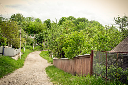 A country road in an old traditional  village with thatched houses, trees and wooden fences.