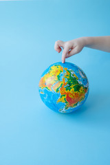 Children's finger shows place on globe sho standing against blue background
