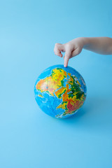 Children's finger shows place on globe sho standing against blue background