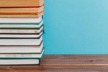A simple composition of many hardback books, raw books on a wooden table and a bright blue background. Going back to school. Copy space. Education.